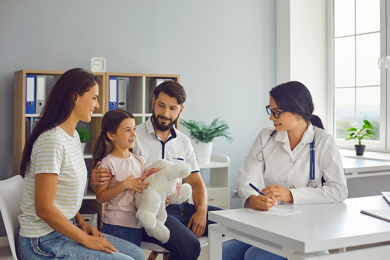 Happy Family in Modern Pediatrician's Office Consulting Friendly Young Female Doctor